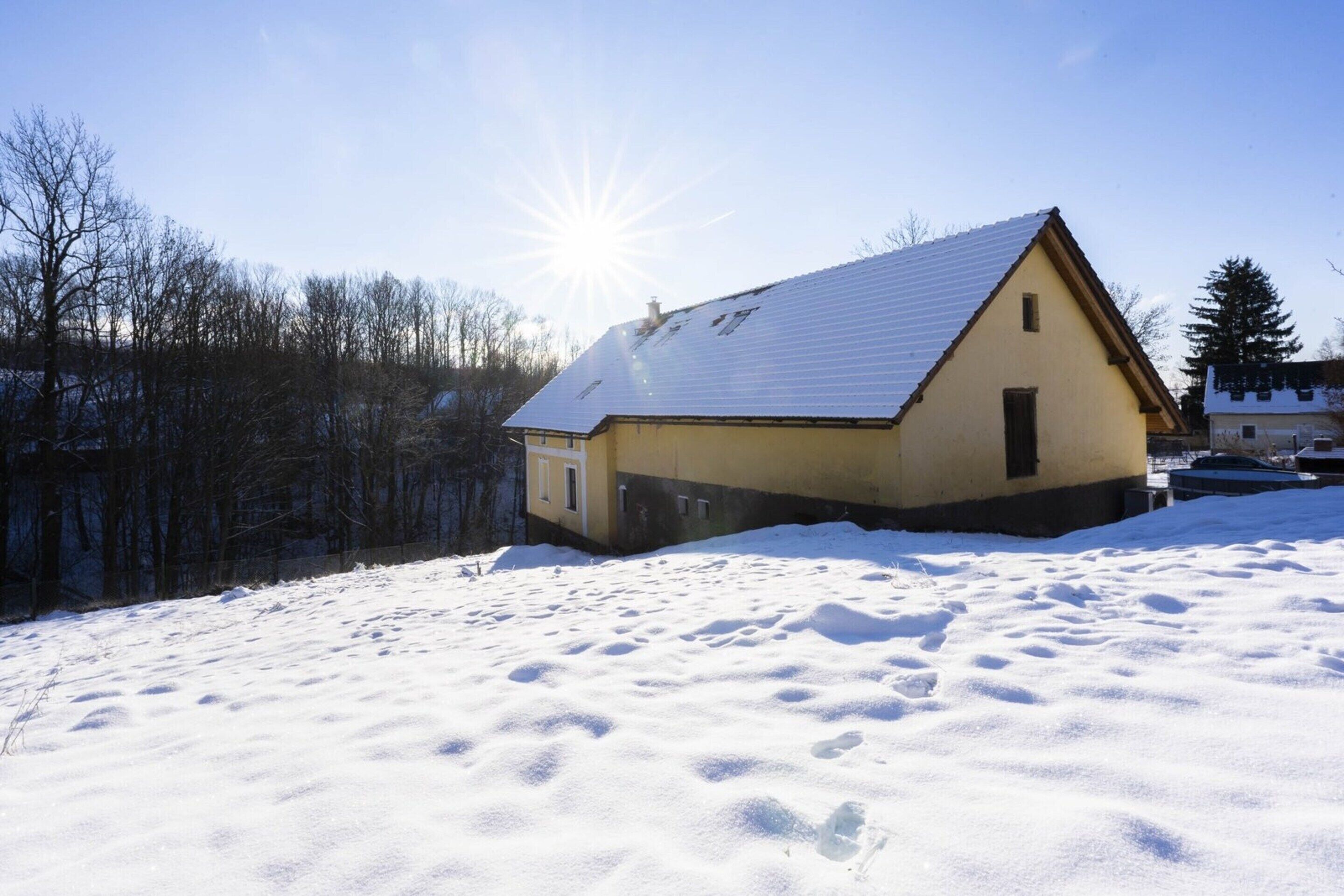 A snow-covered landscape with a single house featuring a gabled roof and a chimney.