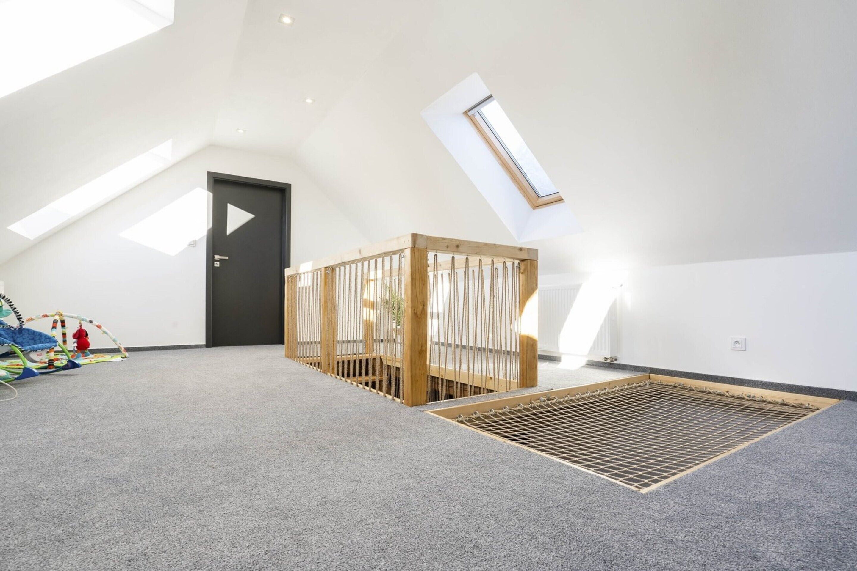 A spacious room with a sloped ceiling, a skylight, a wooden crib, and a play area with toys.