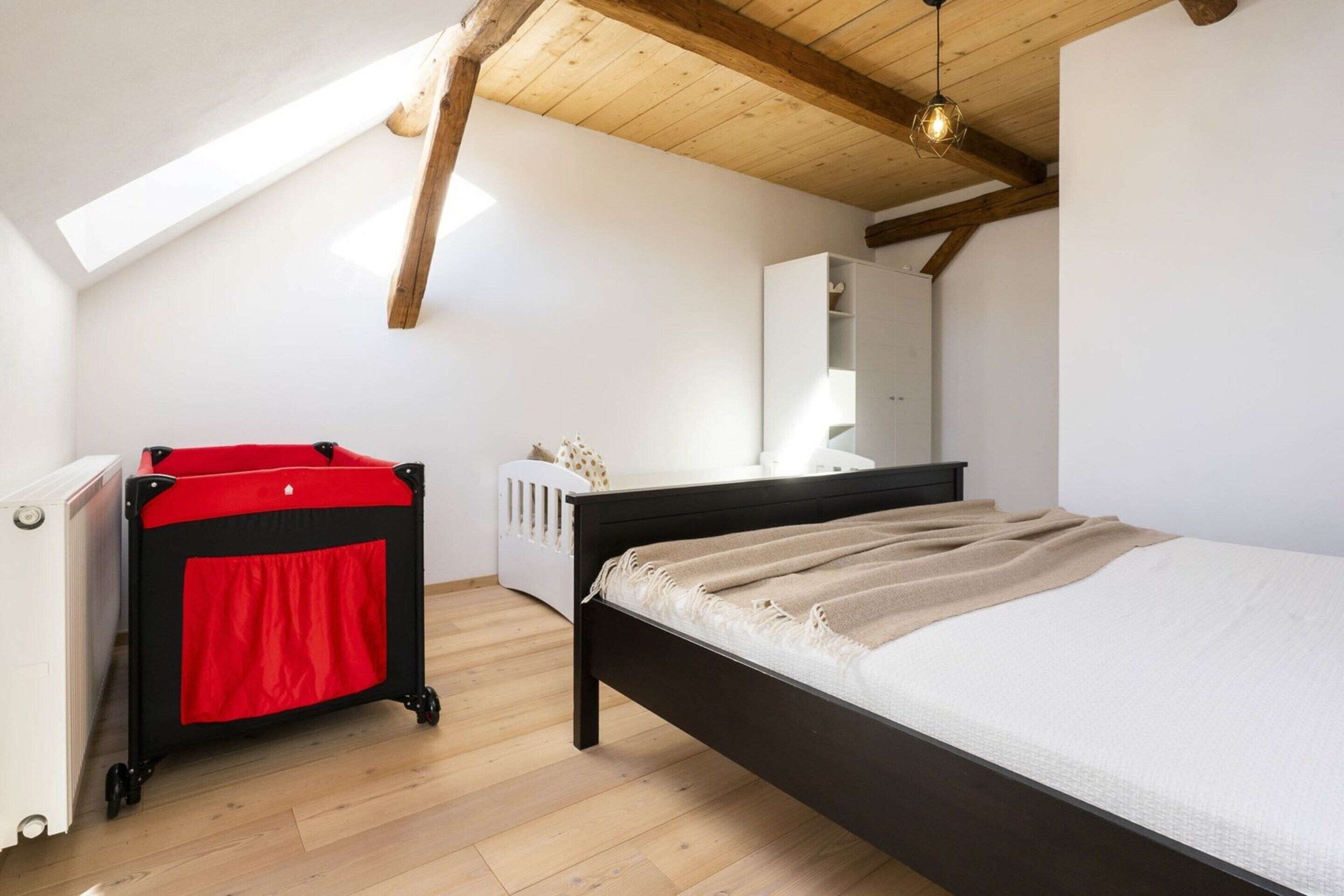 Una camera da letto con un letto, un carrello rosso e nero, un termosifone bianco e un soffitto in legno.