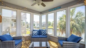 A sunroom with wicker furniture, large windows, and a view of the water. - Canalfront home w/ wraparound decks and community amenities! (Kill Devil Hills)