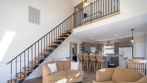 A spacious living area with a staircase, a kitchen, and a dining area. - Canalfront home w/ wraparound decks and community amenities! (Kill Devil Hills)