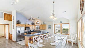 A spacious kitchen with wooden cabinets, a stainless steel refrigerator, and a large island with bar stools. - Oceanside home in Duck NC with private mini golf course! (Duck)