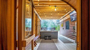 Interior de una cabaña de madera con hidromasaje, bancos de madera y luces colgantes.