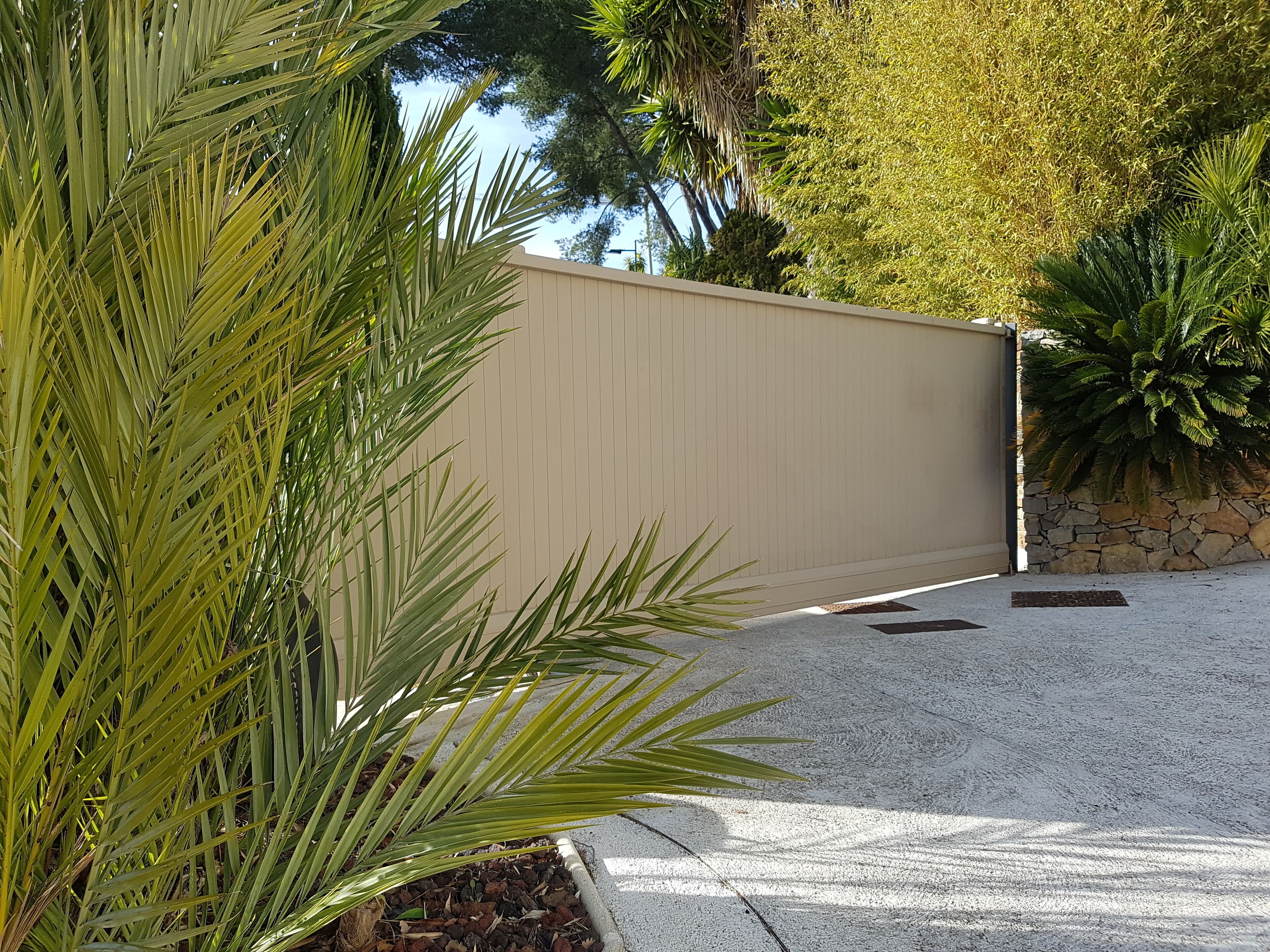 Un camino de entrada con puerta, una palmera y un muro de piedra.