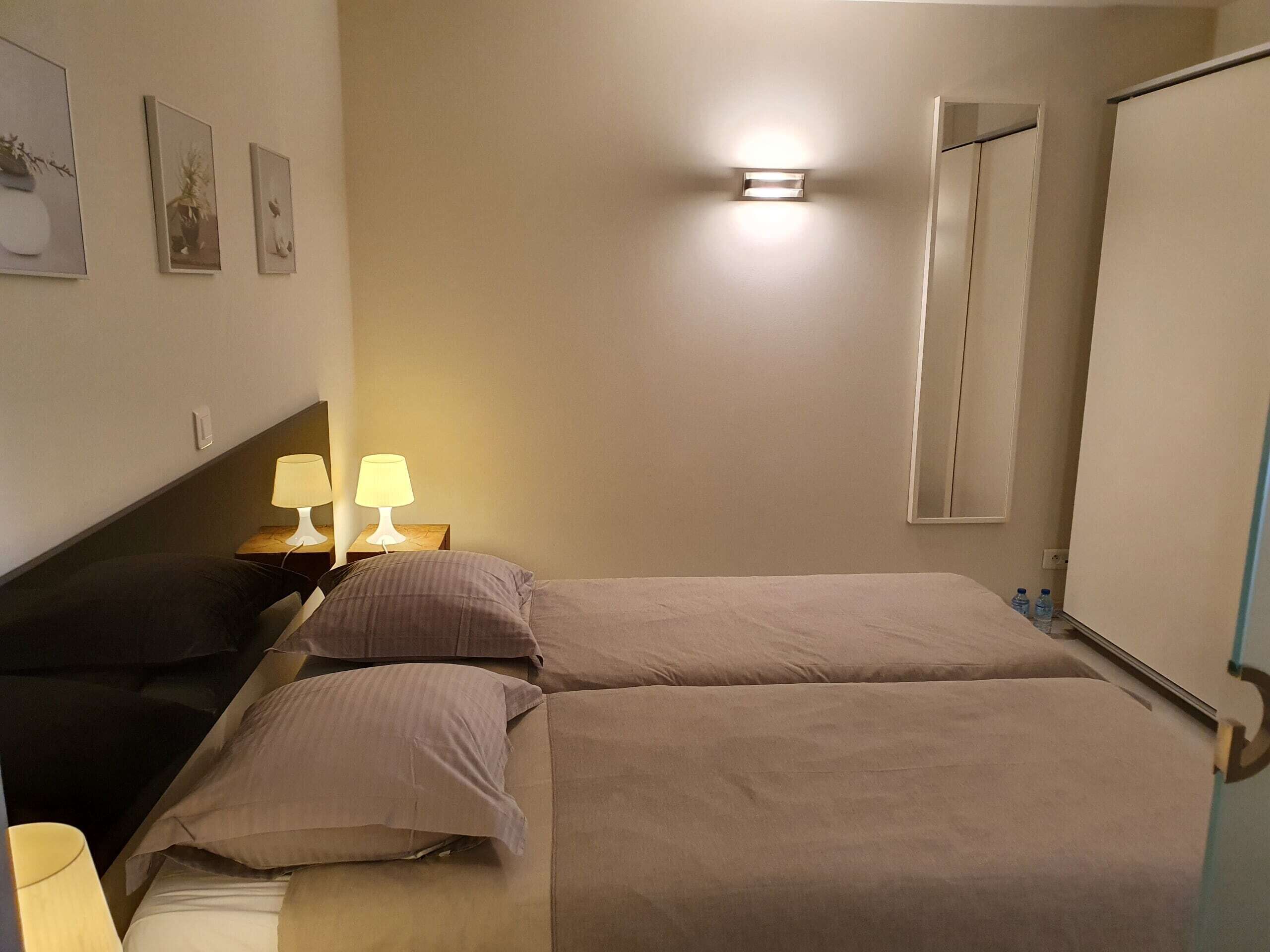 Ett sovrum med två sängar, ett sängbord med lampor, en vägglampa och en spegel.
