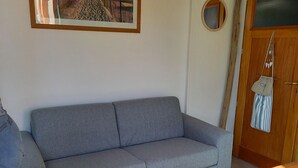 Ein Wohnzimmer mit grauem Sofa, einem Holztisch und einer Tür, an der ein gestreiftes Handtuch hängt.