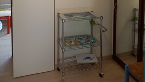 Ein Zimmer mit einem Bett, einem Metallwagen voller Spielzeug, einem Bild an der Wand und einer Tür mit Spiegel.