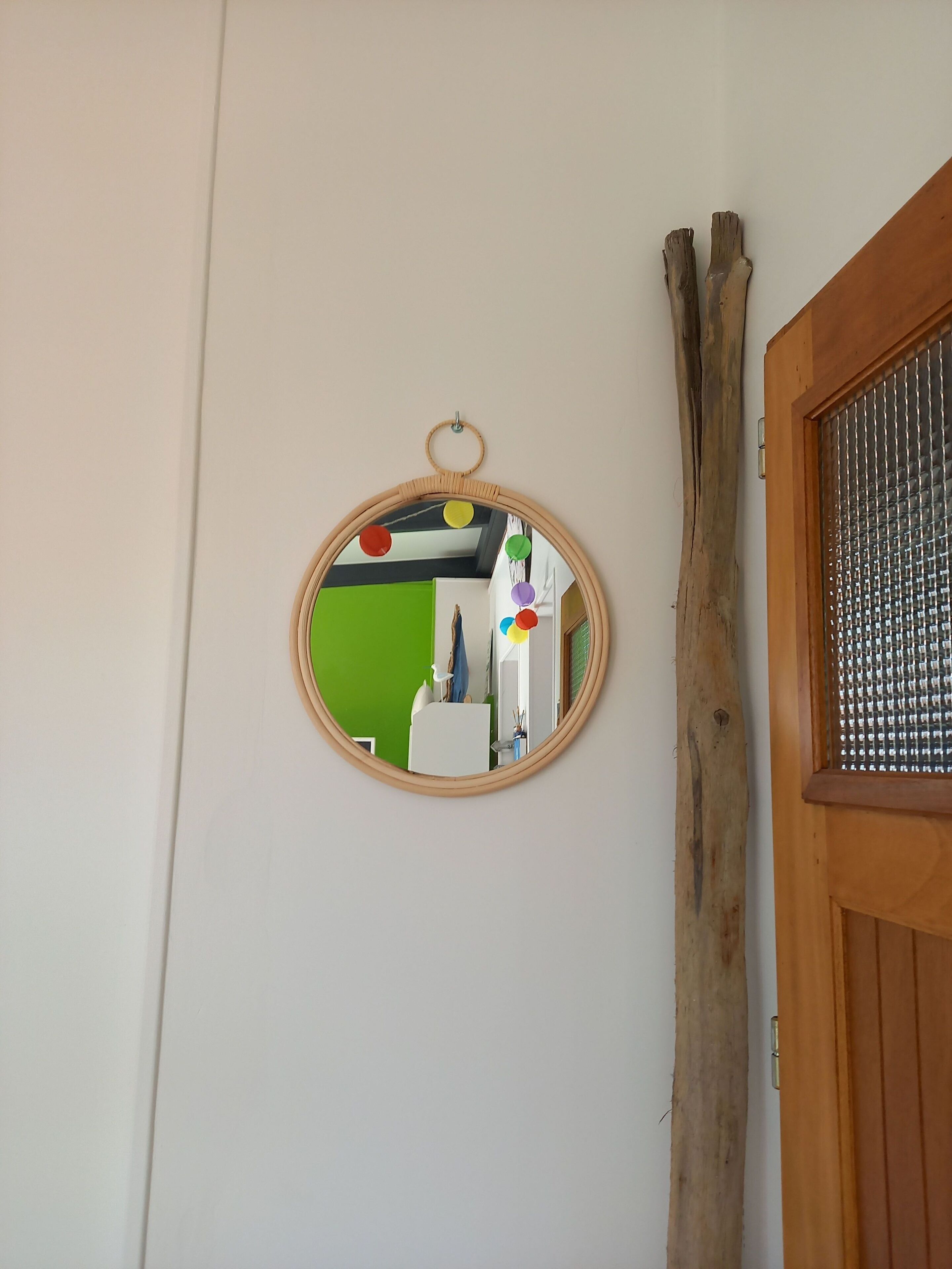 A round mirror on a white wall, reflecting a room with a green wall and a white door.
