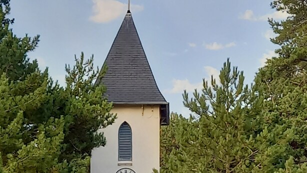 Eine Kirche mit einem Glockenturm, ein Wegweiser mit Beschilderung zu nahegelegenen Orten und zwei Radfahrer.