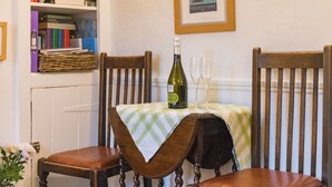 A dining table with a bottle of wine and two glasses, surrounded by wooden chairs. - Claire's Cottage, Hythe (Hythe)