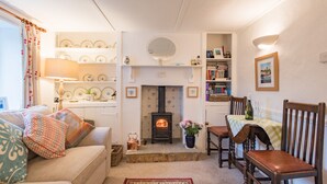 A cozy living room with a fireplace, a sofa, a dining table with chairs, and shelves with decorative items. - Claire's Cottage, Hythe (Hythe)