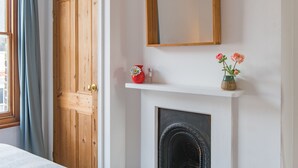 A room with a wooden door, a fireplace, and a shelf with flowers.