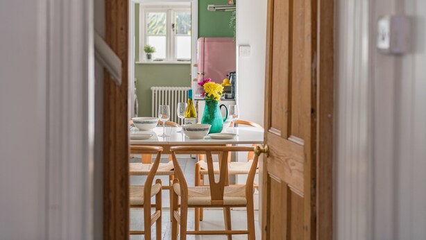 A dining area with a wooden table and chairs, a vase with flowers, and a window with a view of the outside.