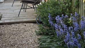 A wooden deck with wicker chairs, a wooden fence, and a garden with purple flowers.
