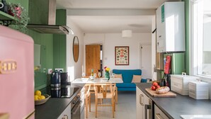 A modern kitchen with a dining area, green walls, and a blue sofa.