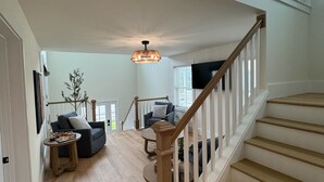 A spacious living area with a wooden staircase, a ceiling fan, and a large TV.