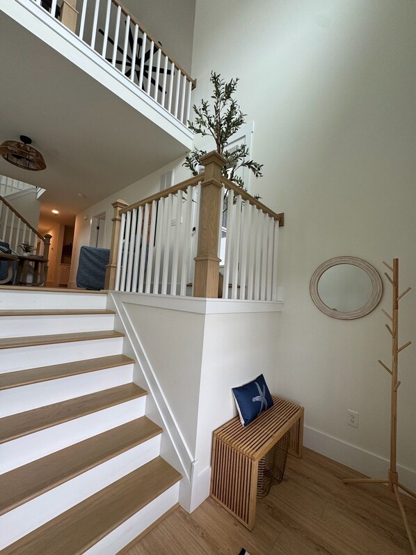 A staircase with white railings and wooden steps, a wooden bench with a cushion, a mirror on the wall, and a plant on the railing. - Plan your getaway in our new 5-bedroom home in welcoming Bethany Beach. (Bethany Beach)