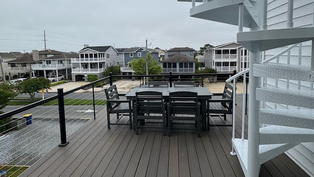 A wooden deck with a table and chairs, overlooking a residential area with houses and a beach.