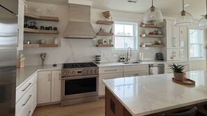 A modern kitchen with white cabinetry, a central island, pendant lights, and a large stove.