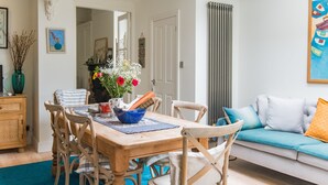A dining area with a wooden table, chairs, and a vase with flowers. There is a sofa with cushions in the background. - Warwick Villa, Walmer (Walmer)
