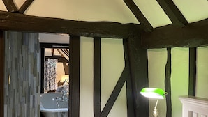Een slaapkamer met een bed, een nachtkastje met een lamp, en uitzicht op een badkamer met een wastafel en spiegel.