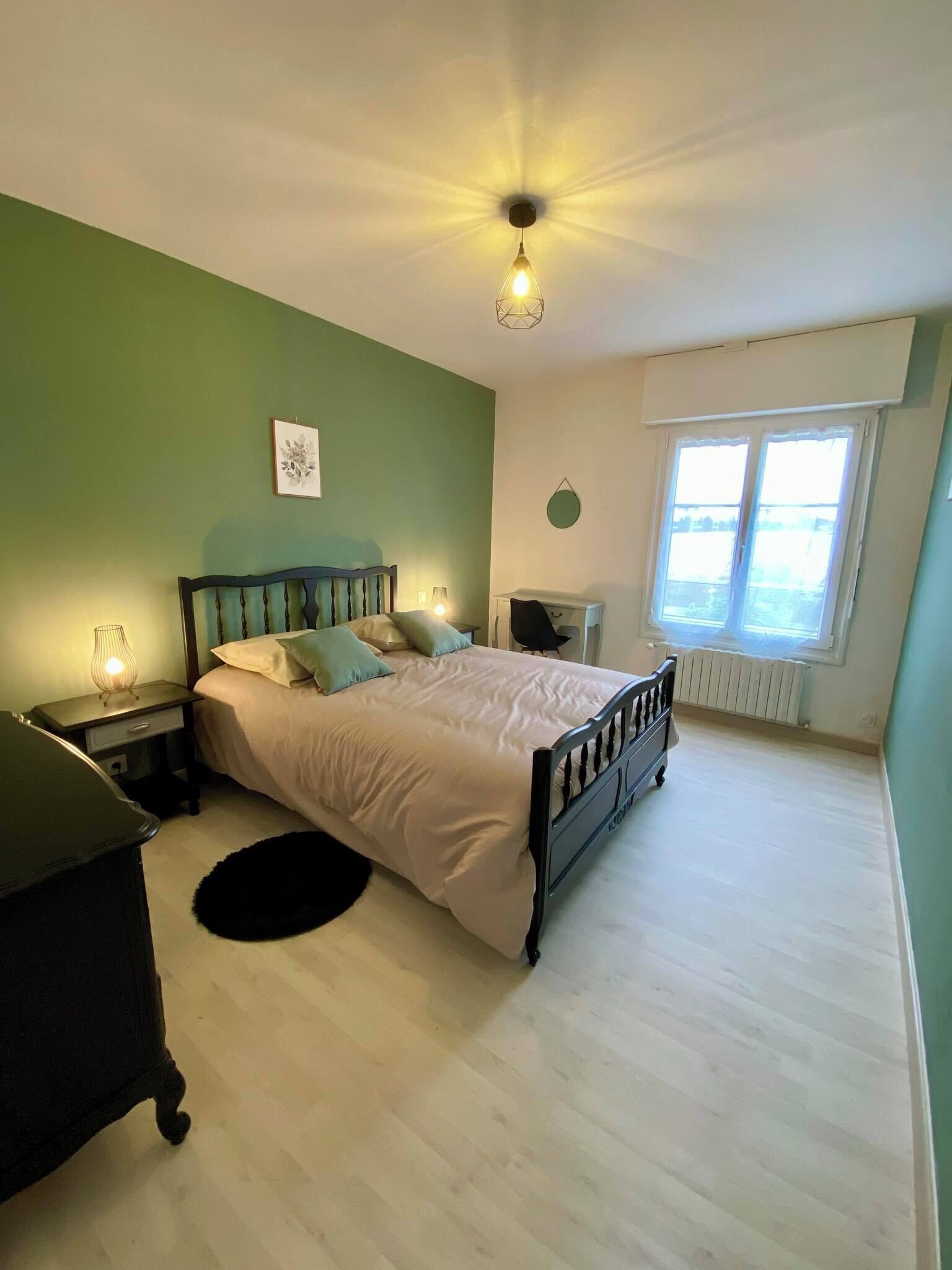 Un dormitorio con cama, mesitas de noche, cómoda, radiador y ventana con cortinas.