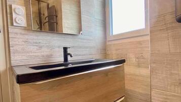 A modern bathroom with a wooden vanity, a black sink, a mirror with lights, and a window.