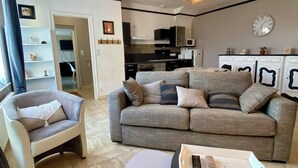 Una sala de estar moderna con un sofá gris, un sillón blanco y una pequeña mesa redonda con un control remoto.