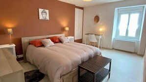 Un dormitorio con cama, mesitas de noche, escritorio, silla, ventana y lámpara de techo.