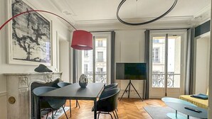 A modern living room with a dining area, a fireplace, a large window with a balcony view, and a flat-screen TV. - Apartment Thorigny - Two Bedroom Villa, Sleeps 6 (Paris)