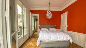 A bedroom with a bed, a chandelier, and a view through a glass door. - Apartment Thorigny - Two Bedroom Villa, Sleeps 6 (Paris)