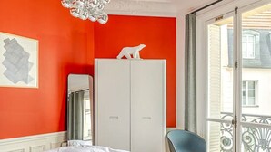 A bedroom with a bed, a wardrobe, a chair, and a balcony with a view of buildings. - Apartment Thorigny - Two Bedroom Villa, Sleeps 6 (Paris)