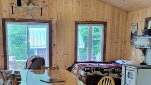 Un coin repas en bois, avec une grande table et des chaises, un lustre et un poêle d’époque.