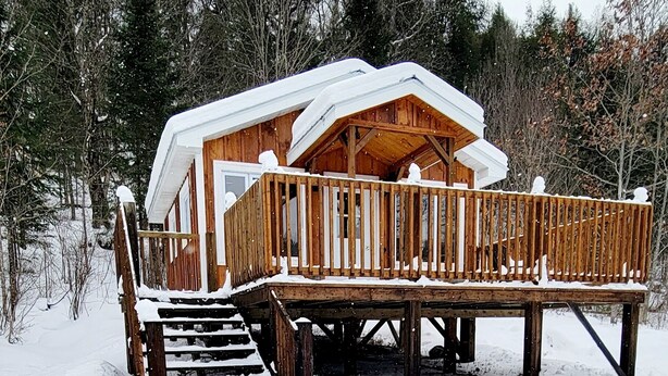 Une cabane en bois dotée d’une terrasse et d’un escalier, entourée de neige et d’arbres.