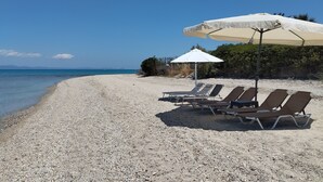 A pebble beach with lounge chairs and a large umbrella.