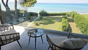 A balcony with a glass table and chairs, overlooking a well-maintained garden and the sea.