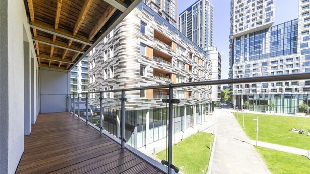 Un moderno edificio de apartamentos con terraza de madera y barandilla de cristal con vista a un patio verde.