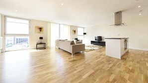 Amplia sala de estar con sofá, televisor y una zona de cocina con mostrador.