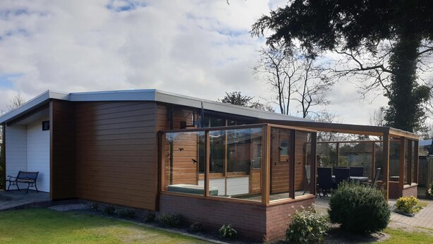 Ett modernt hus med en inglasad uteplats, en träfasad och en liten trädgård.