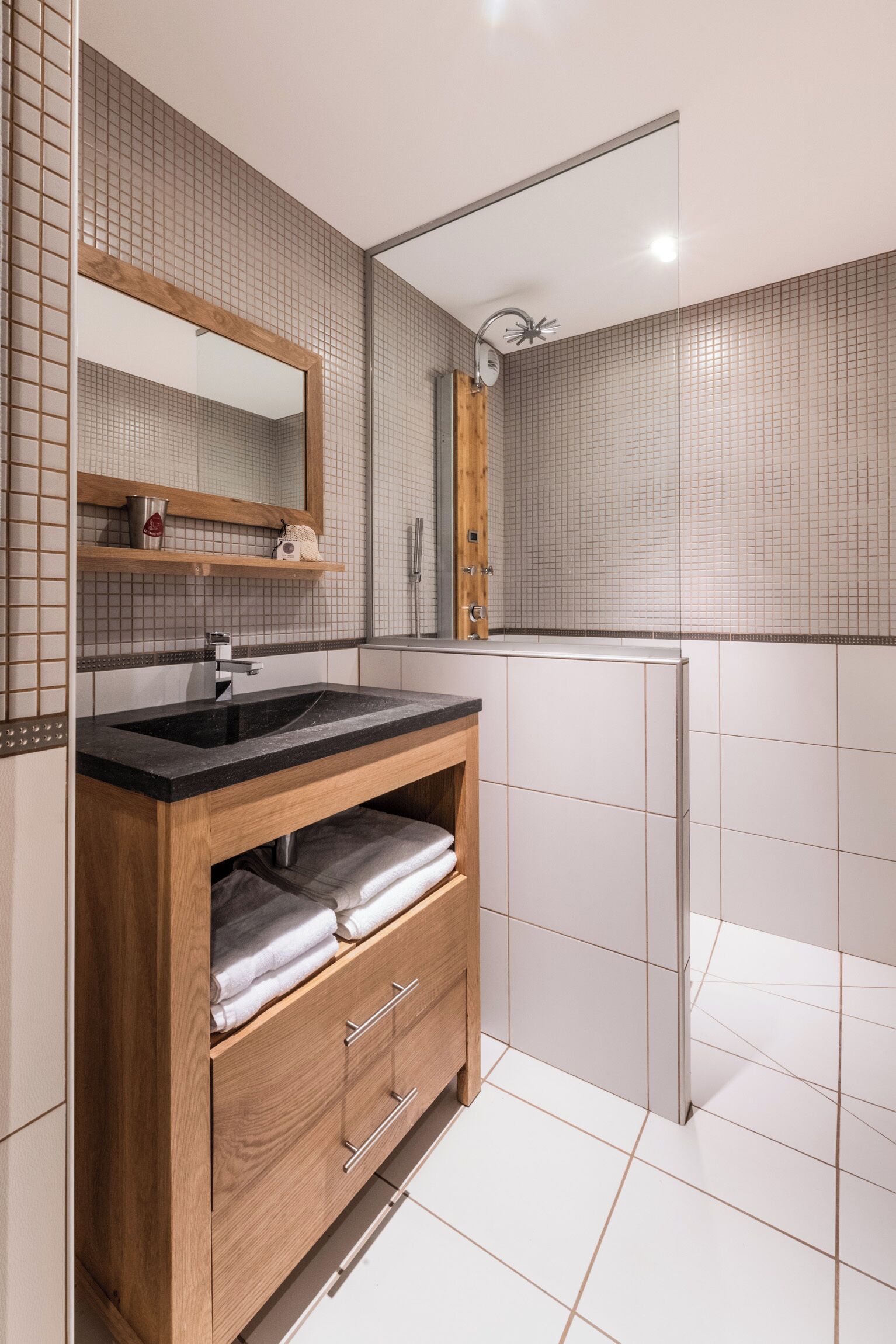 Un baño moderno con tocador de madera, un espejo, ducha y paredes con azulejos.
