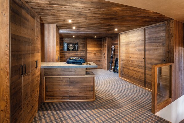 A wooden interior with a checkered floor, a counter with a bag, and skis leaning against the wall.