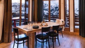 A dining area with a wooden table set for six, large windows, and hanging pendant lights.