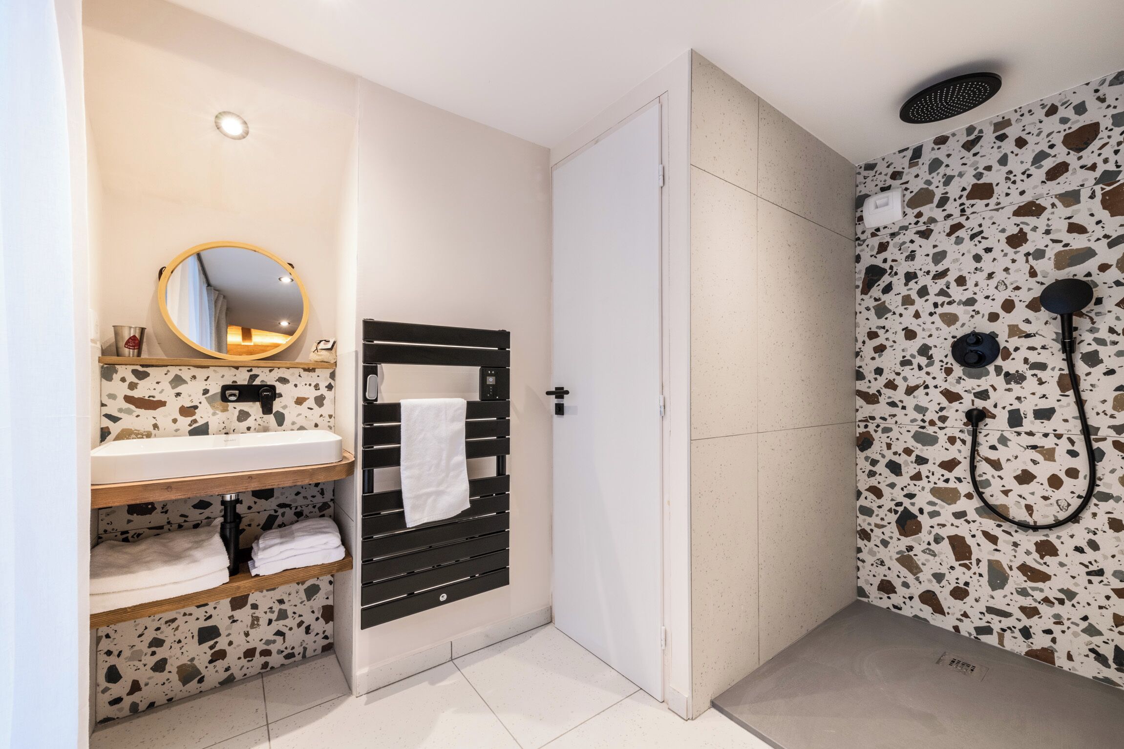 Une salle de bain moderne avec un lavabo blanc, un miroir rond et un porte-serviettes noir.