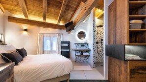 A bedroom with a bed, a TV, a bathroom with a sink and mirror, and wooden beams on the ceiling.