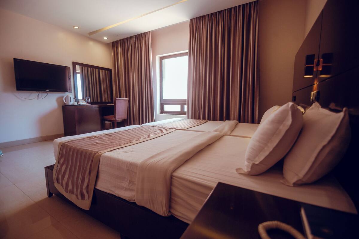A hotel room with a large bed, a desk with a chair, a television, and a window with curtains.