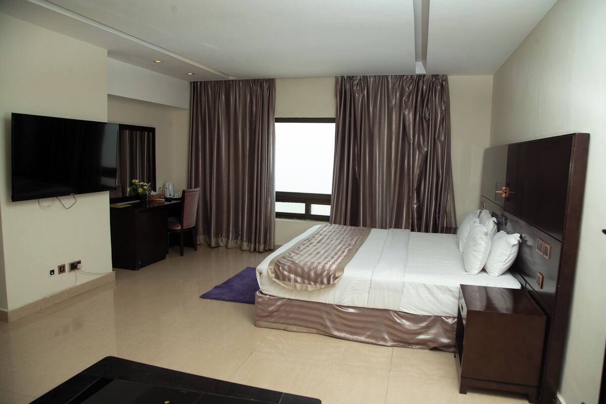 A hotel room with a bed, a desk, a TV, and a window with curtains.