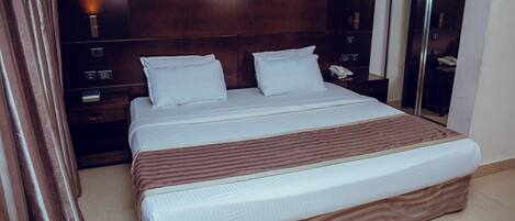 A hotel room with a large bed, wooden headboard, bedside tables, and a mirror.