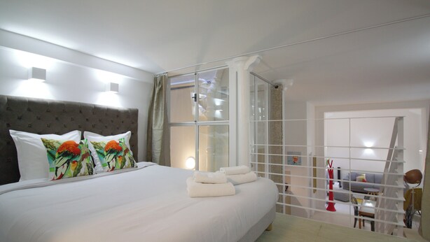 A bedroom with a large bed, a glass partition, and a view of a living area. - 2-bedroom loft in the heart of Paris (Paris)