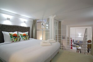 A bedroom with a large bed, a glass partition, and a view of a living area.