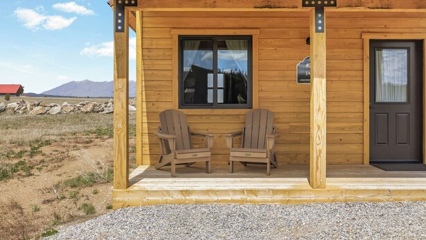 Una cabaña de madera con dos sillas Adirondack en el porche, una ventana y una puerta.